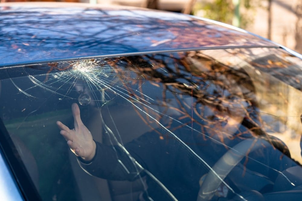 Woman shocked in car with shattered windshield and cracks. A car accident in New Orleans requiring windshield repair. Selective focus.