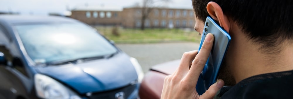 Individual in New Orleans on the phone discussing a recent car accident, street scene in the background.