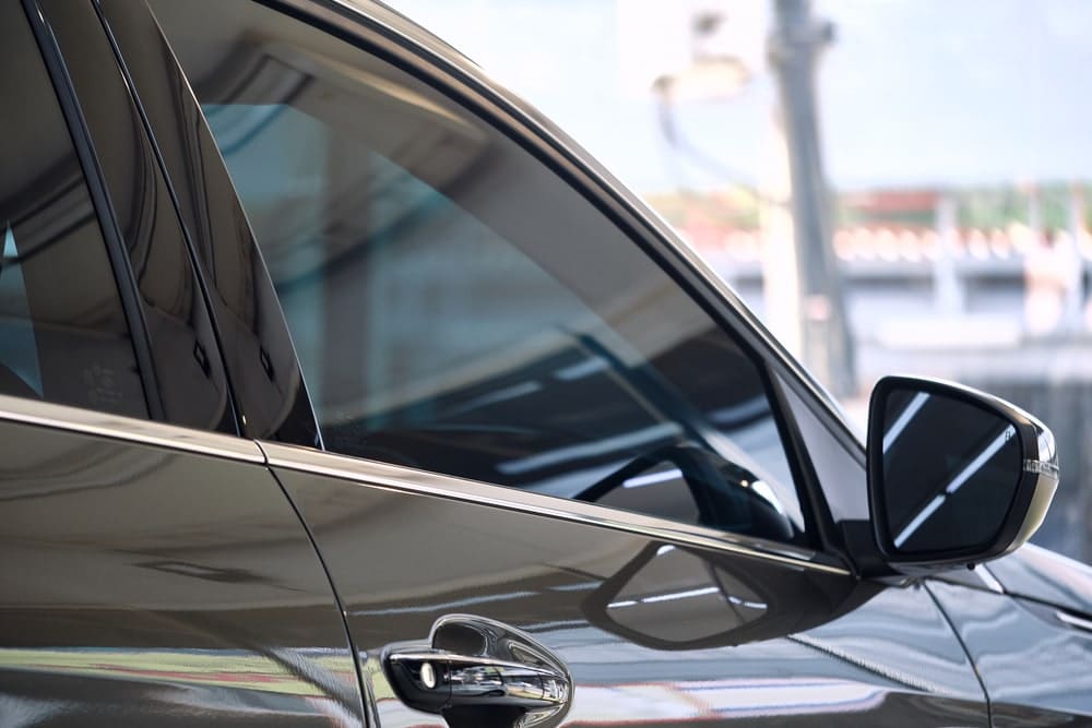 Close-up of a car's window with ceramic tinting film, providing UV shielding and thermal rejection on a red car's glass.