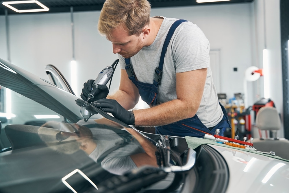 Car service technician checks crack on car windshield closeup, doing windshield repair