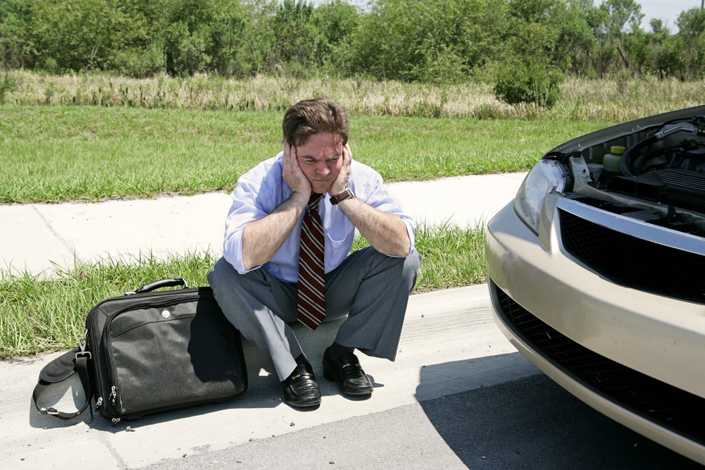 A concerned driver beside their vehicle, seeking assistance for a cracked windshield, awaiting expert auto glass repair services.
