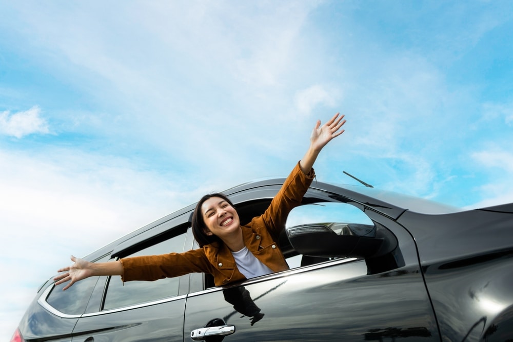 Smiling female driving vehicle on the road on a bright day - auto glass repair new orleans